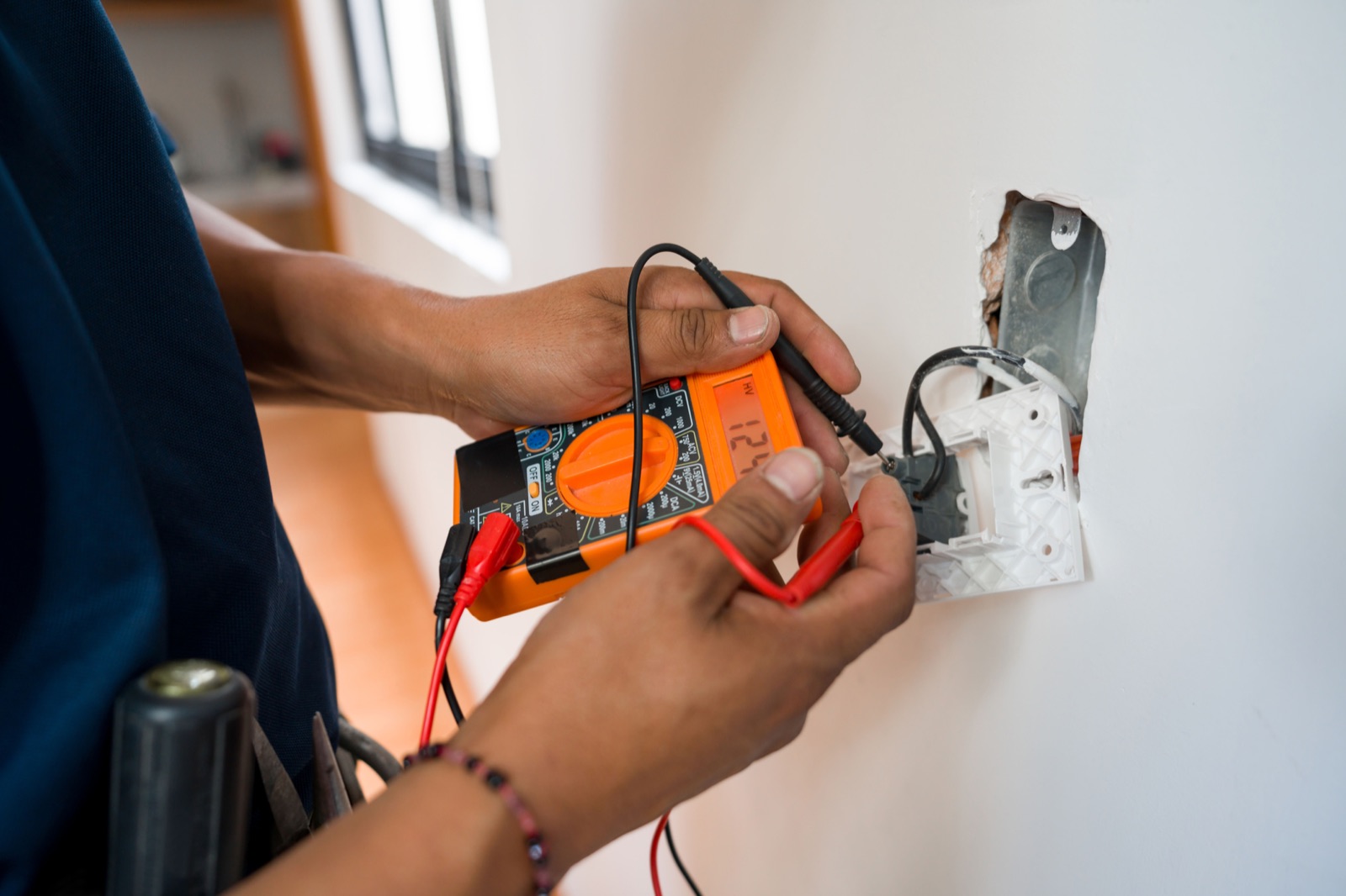 Electrician testing a wall outlet with a multimeter during electrical troubleshooting in Baltimore MD